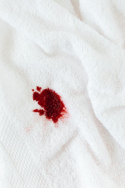 Close-up of a white fabric surface, likely a towel or cloth, with a small, irregularly shaped red stain in the center indicating a recent spill or stain. The fabric appears clean and well-maintained, with visible textured weaves. The background is plain, emphasizing the stain's position and color. This image highlights the importance of surface cleaning and stain removal in domestic or commercial environments. For effective stain treatment, professional cleaning services by Carpet Cleaner Fulham offer expert solutions for fabric and surface sanitisation, ensuring hygiene and cleanliness are maintained,